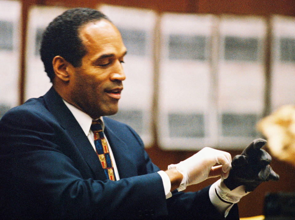 يرتدي OJ Simpson قفازات مطاطية ويبدو أنه يحاول سحب قفاز جلدي أسود فوق يده اليسرى.
