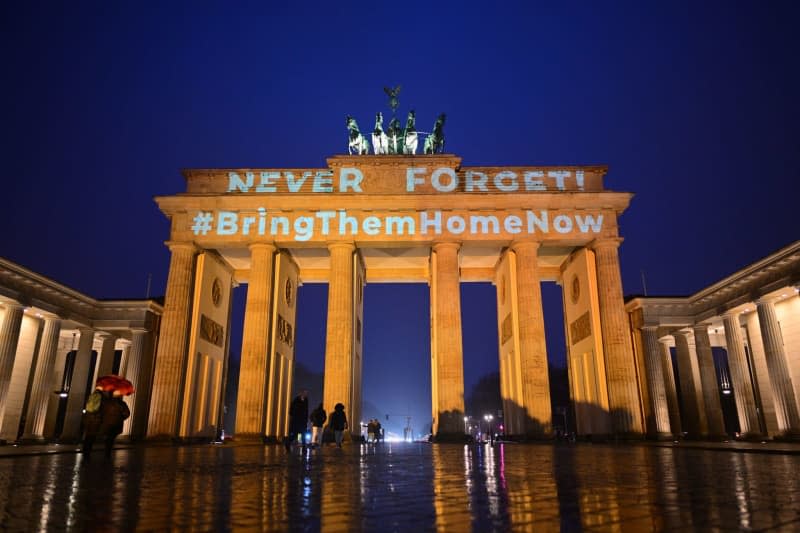 يتم عرض الكلمات "لا تنسى أبدًا" و "#BringTheMhomenow" على بوابة براندنبورغ البرتقالية خلال خدمة تذكارية للاحتفال بجنازة أفراد عائلة بيباس في إسرائيل. سيباستيان كريستوف جولنو/DPA