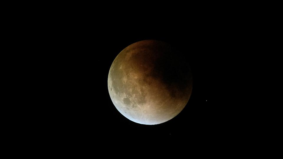 الكسوف القمري مع ظل أحمر غامق في الجزء العلوي الأيمن من القمر ولون أبيض فاتح في أسفل اليسار.