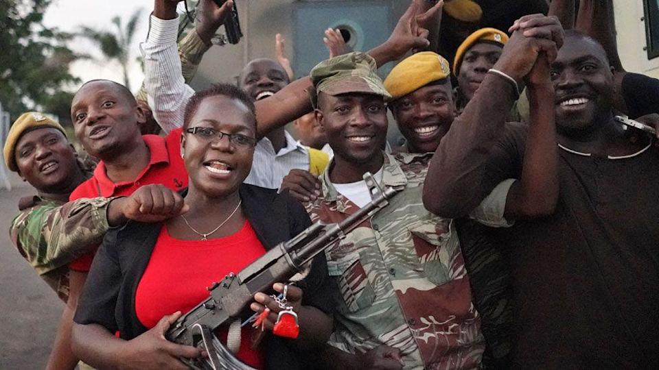 يحتفل Zimbabweans مع الجنود في الشارع بما في ذلك امرأة في قميص أحمر وأسران أسود يحمل مدفع رشاش في عام 2017