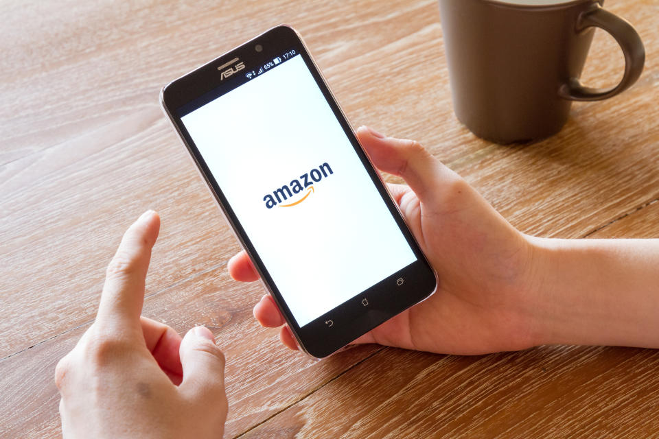 يدويًا يمسك هاتفًا محمولًا مع تطبيق Amazon Shopping على الشاشة