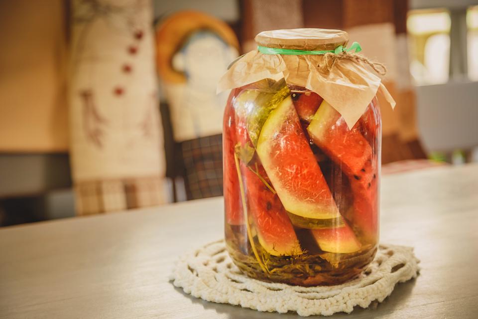 البطيخ المتبل أو المخلل مع الأعشاب في جرة زجاجية على طاولة خشبية في المطبخ.