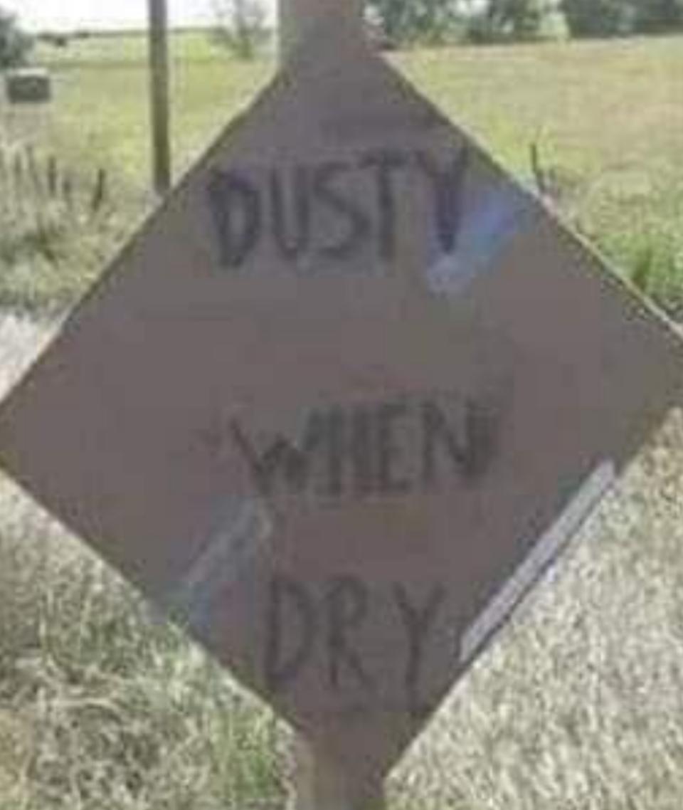 تقرأ علامة الطريق على طريق ريفي "Muddy عندما تكون رطبًا" و "Dusty عندما تجف" ، مع تسليط الضوء على الظروف المختلفة بناءً على الطقس