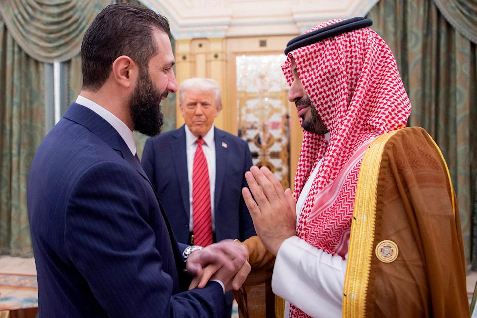 ولي العهد السعودي الأمير محمد بن سلمان يهز يديه الرئيس المؤقت في سوريا أحمد الشارا كما ينظر الرئيس الأمريكي دونالد ترامب. (Bandar al-Jaloud / AFP عبر Getty Images)