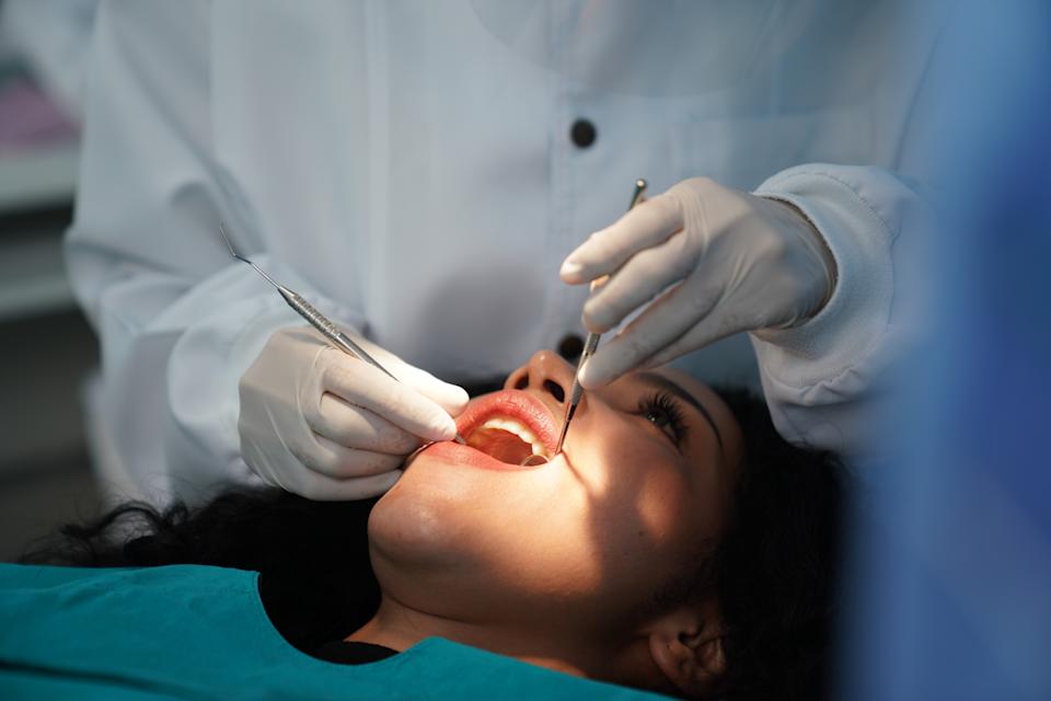 شخص يرقد على كرسي طب الأسنان يتلقى امتحان طب الأسنان من قبل قفازات يرتدي معطفًا أبيض