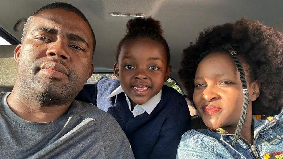 يطرح Sipho (L) و Sibahle Mbasana للكاميرا في سيارتهما مع ابنتهما Buhle ، في Jumper Navy وزي قميص أبيض ، يبتسم بينهما وهي تميل من المقعد الخلفي.