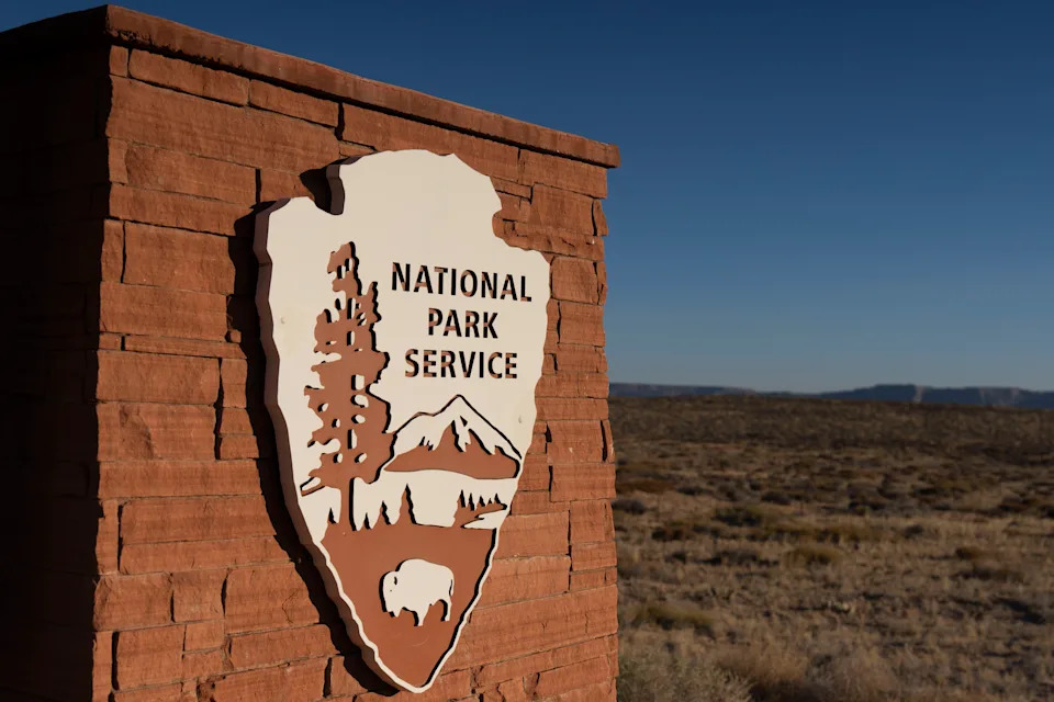 شعار National Park Service Shield على علامة حجرية في مشهد صحراوي واسع