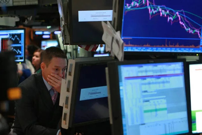 يظهر متداول الأسهم قلقًا أثناء النظر إلى العديد من الشاشات التي تعرض الرسوم البيانية لسوق الأسهم المتقلبة في أرضية تداول مزدحمة
