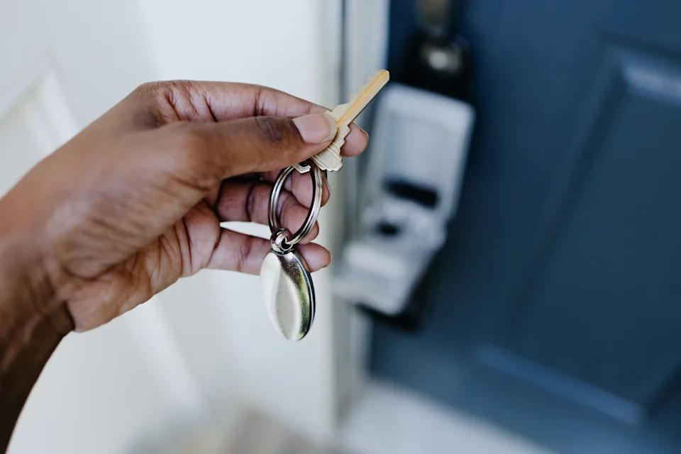 يد تحمل مفتاحًا وسلسلة مفاتيح أمام قفل الباب ، ترمز إلى ملكية المنازل أو الاستثمار العقاري
