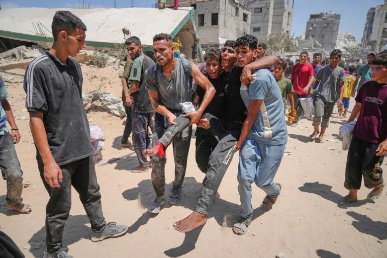 يحمل الفلسطينيون رجلاً أصيب بجروح أثناء اندفاعه لجمع المساعدات الإنسانية التي قام بها المظلة إلى مدينة غزة ، في قطاع غزة الشمالي ، الخميس ، 7 أغسطس ، 2025. (AP Photo/Jehad Alshrafi)