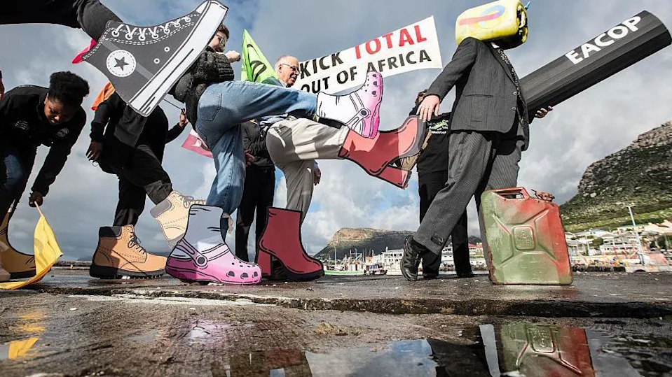 المتظاهرون يسيرون على طول الشاطئ يحملون أعلام تمرد الانقراض وراية مع الكلمات التالية المكتوبة عليها "ركل إجمالي من إفريقيا". يقوم المتظاهرون بتقديم طلبات الركل ولديهم أحذية وهمية كبيرة - الثلاثاء 19 أغسطس 2025.