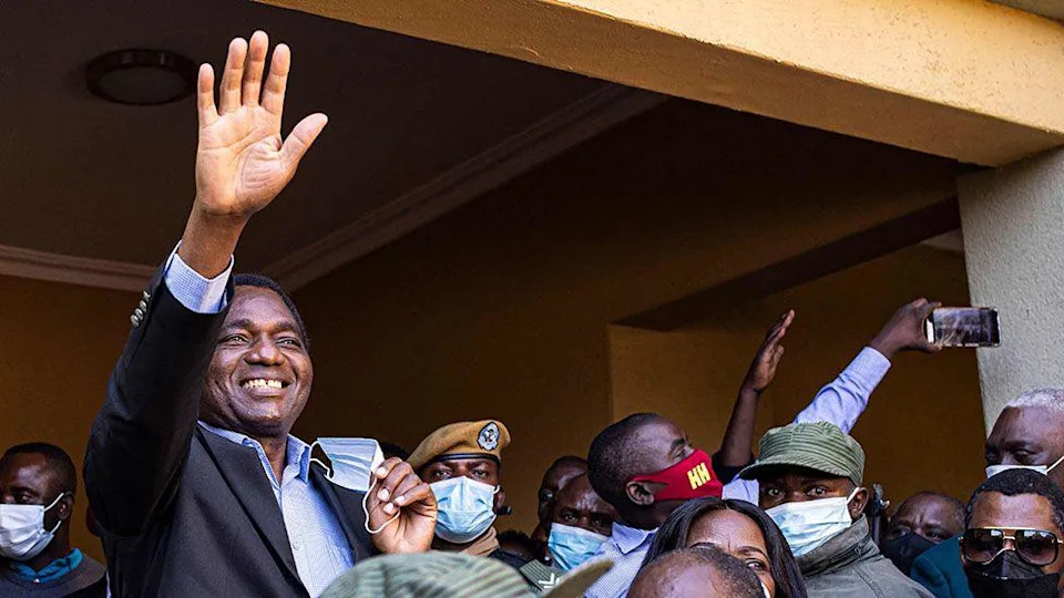 Hakainde Hichilema في قميص أزرق مفتوح وابتسام السترة المظلمة والأمواج على مؤيديه.