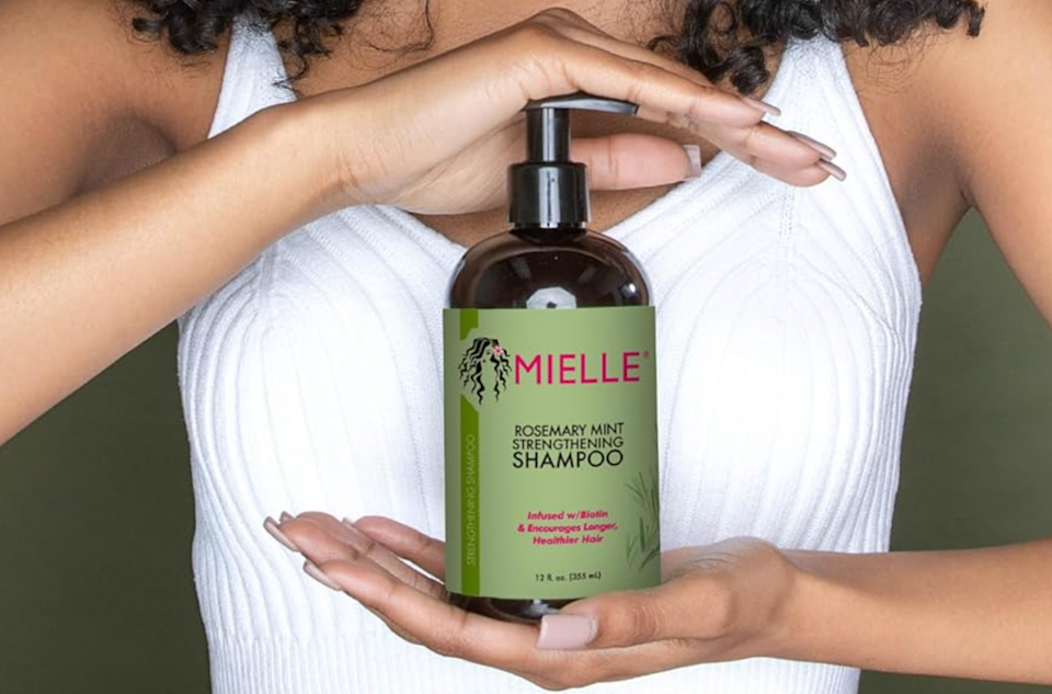 الشخص الذي يحمل Mielle Organics Rosemary Mint تقوية الشامبو بين يديها
