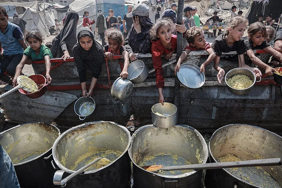 يحاول الفلسطينيون ، بمن فيهم الأطفال ، تلقي وجبات ساخنة ، وزعت من قبل المنظمات الخيرية ، حيث يكافح الناس للوصول إلى الطعام بسبب الحصار الغذائي الإسرائيلي في مدينة غزة ، غزة. / الائتمان: عبدكيم أبو ريش/ anadolu عبر Getty Images