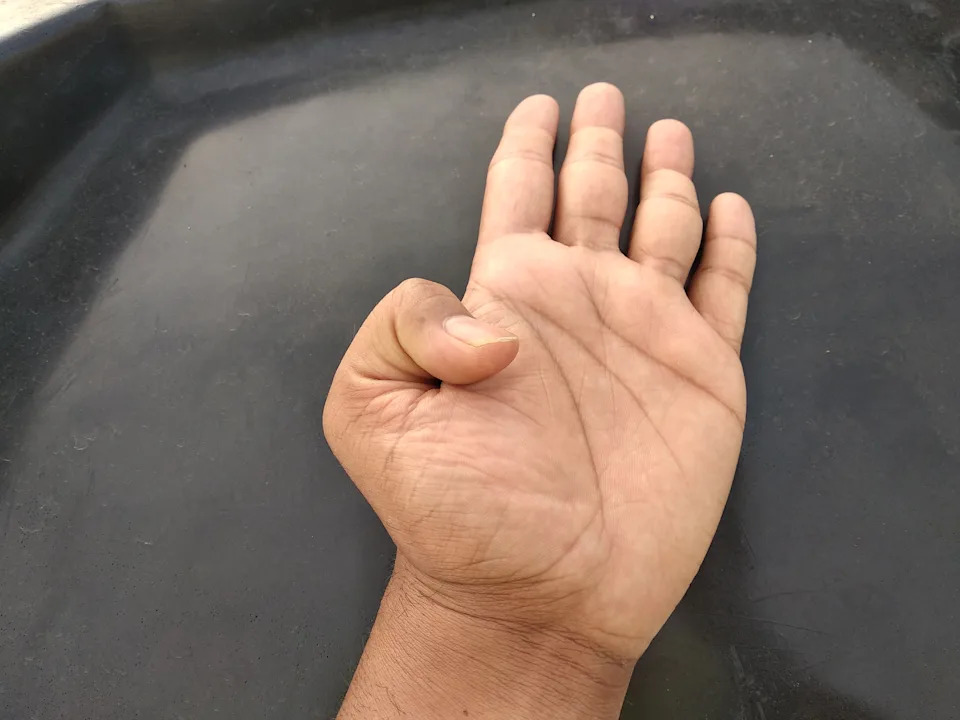 يدًا تعرض إبهام Hitchhiker ، وتستريح على سطح مظلم مع أصابع تنتشر قليلاً