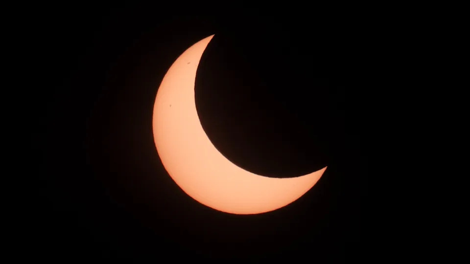 يتم تصوير قرص الشمس خلال كسوف شمسي جزئي مع ثلثين من الجانب الأيمن العلوي المخبأ بواسطة صورة ظلية منحنية من قمر الأرض على سماء مظلمة ، تاركًا فقط هلالًا متوهجًا.