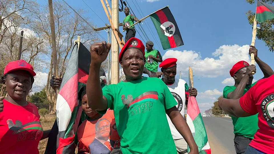 مؤيدو Lazarus Chakwera's MCP على جانب الطريق. الرقم الرئيسي في المركز هو عقد قبضته وارتداء تي شيرت حزب أخضر و BERET الأحمر. البعض الآخر يلوح بأعلام الحزب.