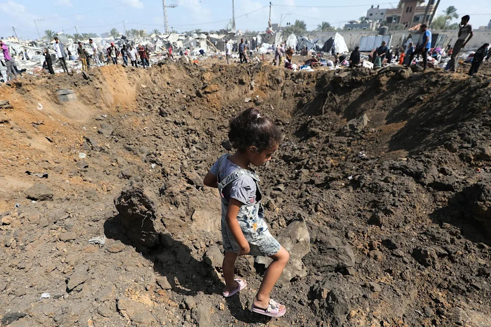 تسير فتاة فلسطينية نازحة بجانب حفرة التأثير ، التي تركت وراءها بعد ضربة إسرائيلية ، في معسكر للمنزل داخليًا في دير الاله في قطاع غزة الوسطى (AFP/Getty)