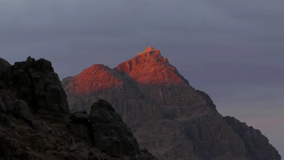 ذروة جبل سيناء عند الغسق في عام 2024. يمسك الضوء بأعلى الجبل الصخري ، الذي يقف أعلى من جبل آخر في المقدمة