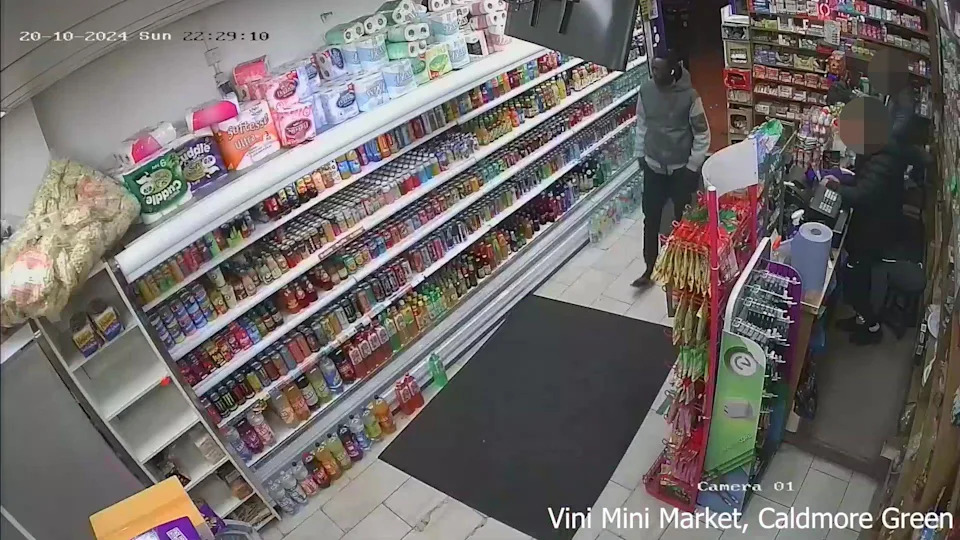 لقطة شاشة مأخوذة من فيديو CCTV الصادر عن شرطة النقل البريطانية، تظهر السيد ماجيك في متجر في كالدمور جرين. الرفوف مبطنة بزجاجات المشروبات وغيرها من المنتجات.