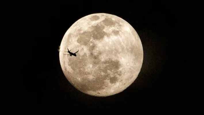 تم تصوير البدر في سماء مظلمة مع ظهور صورة ظلية لطائرة ركاب على يسار قرصها.