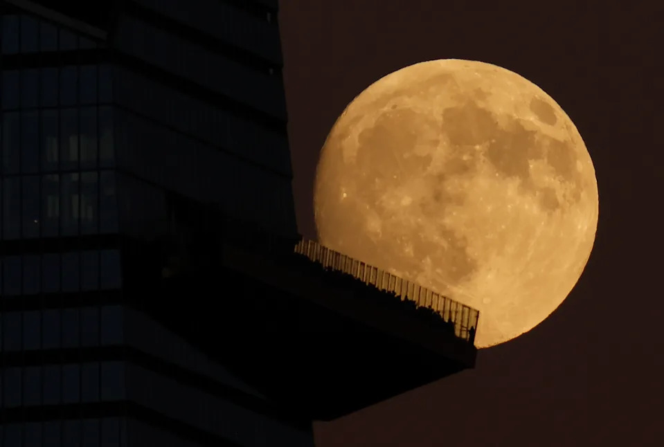 تم تصوير البدر الأصفر وهو يرتفع في سماء مظلمة خلف صورة ظلية لناطحة سحاب، والتي تهيمن على يسار الشاشة.