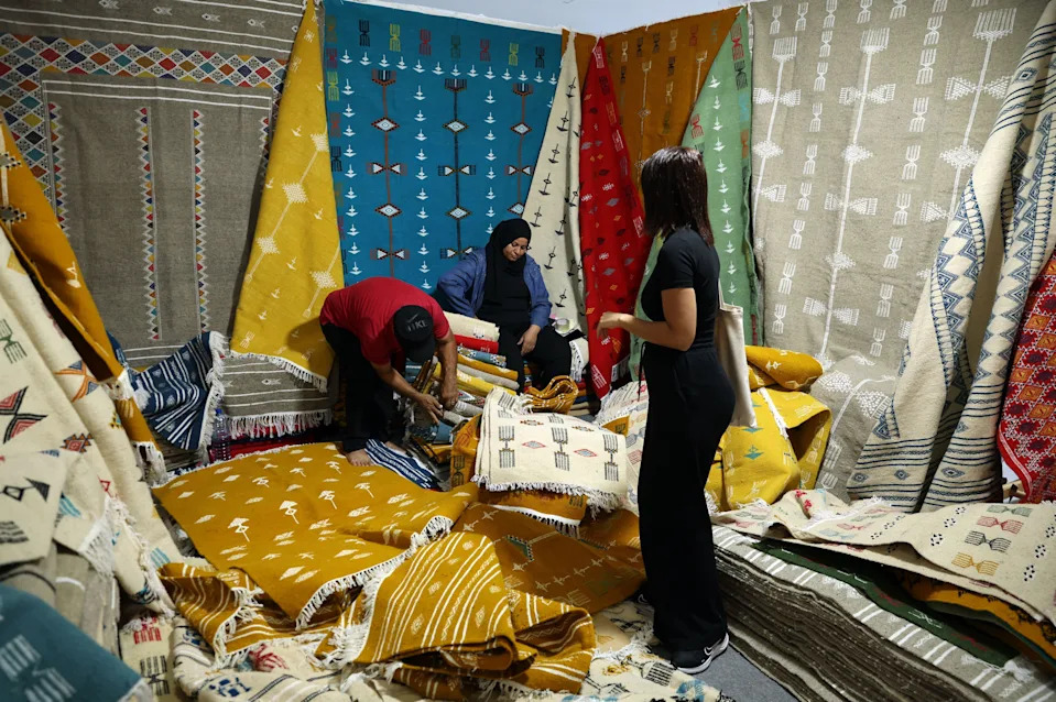 تعرض النساء سجادًا متنوعًا ذو ألوان زاهية للبيع في كشك عرض كبير.