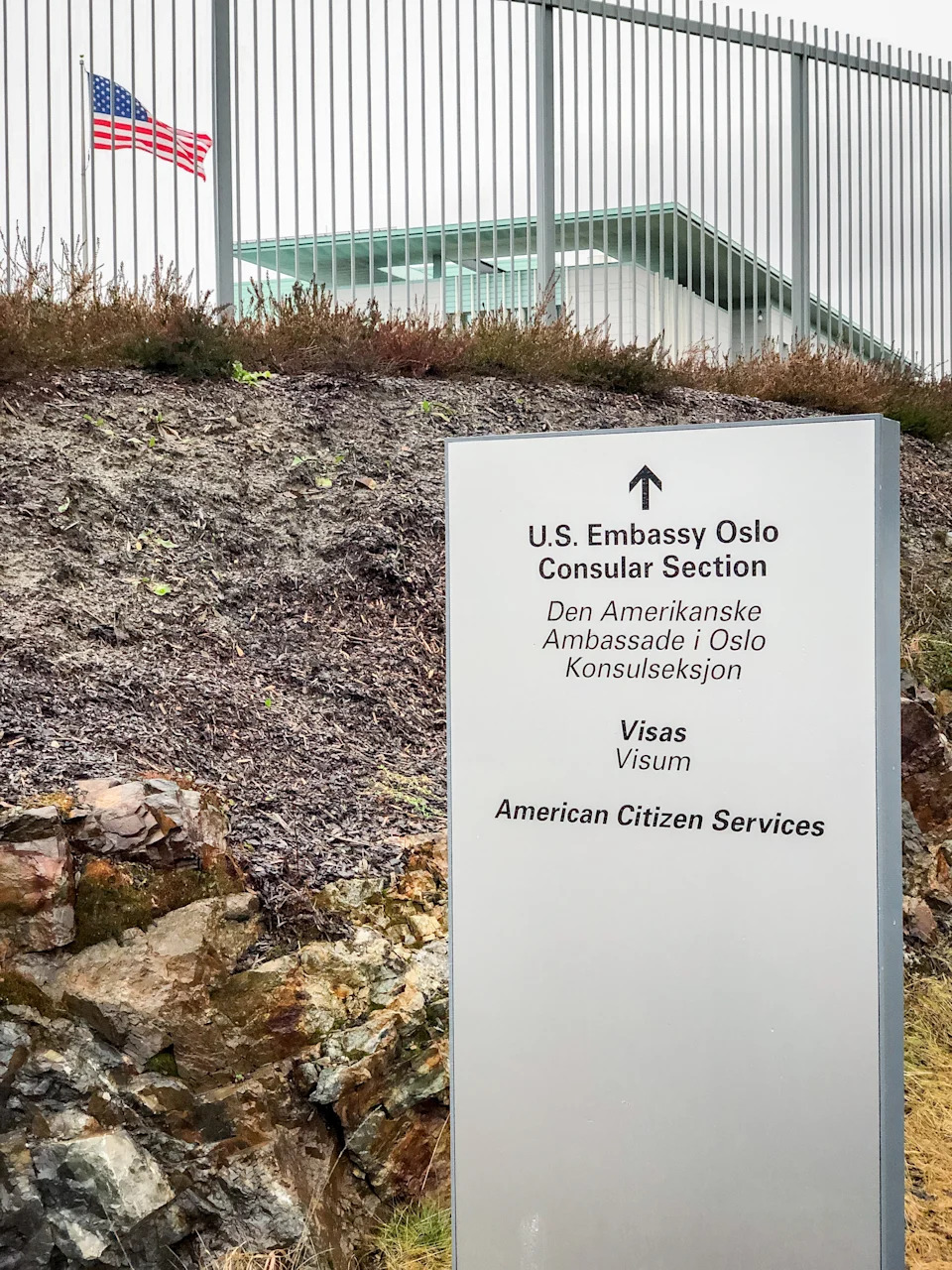 قم بتسجيل القسم القنصلي الخاص بـ Embassy Oslo مع توجيهات لخدمات التأشيرة والمواطنين الأمريكيين. العلم الأمريكي مرئيًا وراءه