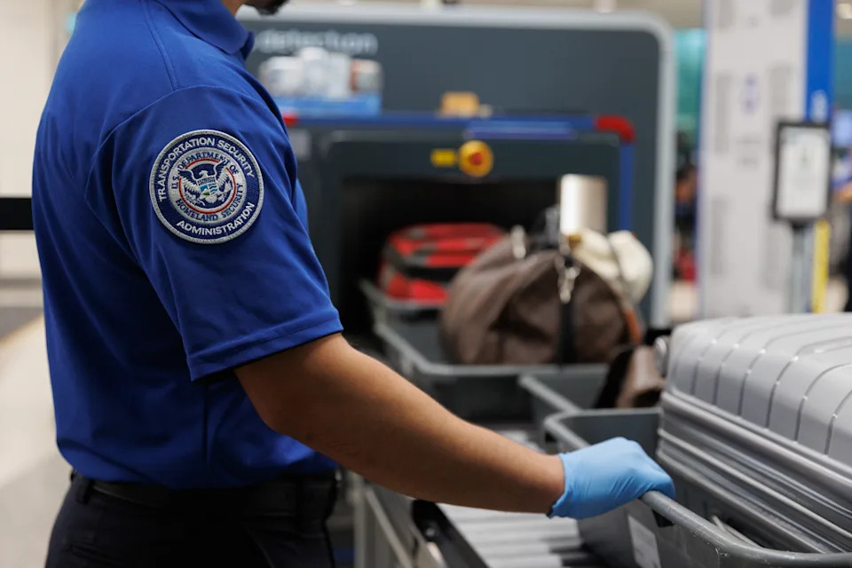 يفحص وكيل TSA بالزي الرسمي الأمتعة في نقطة تفتيش أمن المطار