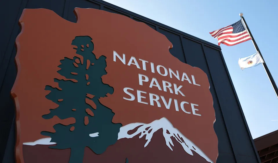 علامة National Park Service مع تصميم الأشجار والجبال ، إلى جانب أعلامنا ومتنزهين تلوح في سماء صافية
