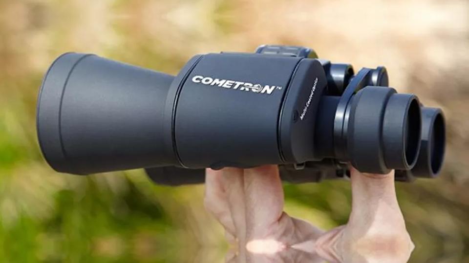 مناظير Celestron Cometron 7x50 تمسك أمام خلفية أوراق الشجر
