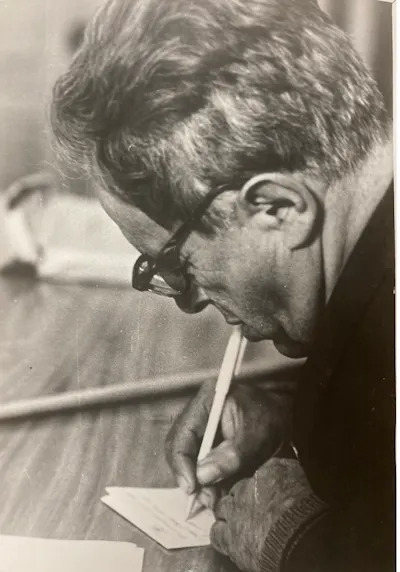 رجل يجلس على مكتب ويكتب بقلم.