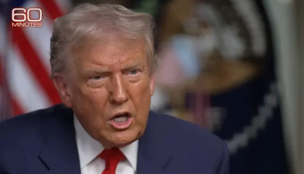 رجل يرتدي بدلة يجري مقابلة جادة حول "60 دقيقة." يظهر العلم الأمريكي في الخلفية