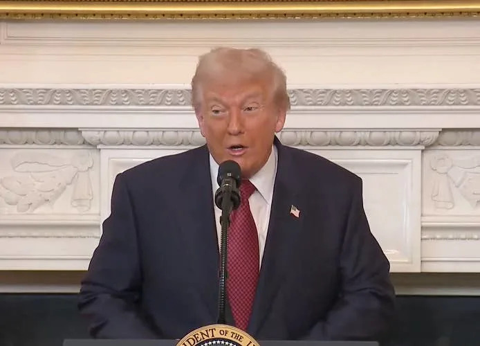 شخص يرتدي بدلة وعليها دبوس العلم الأمريكي ويتحدث على المنصة في إطار رسمي