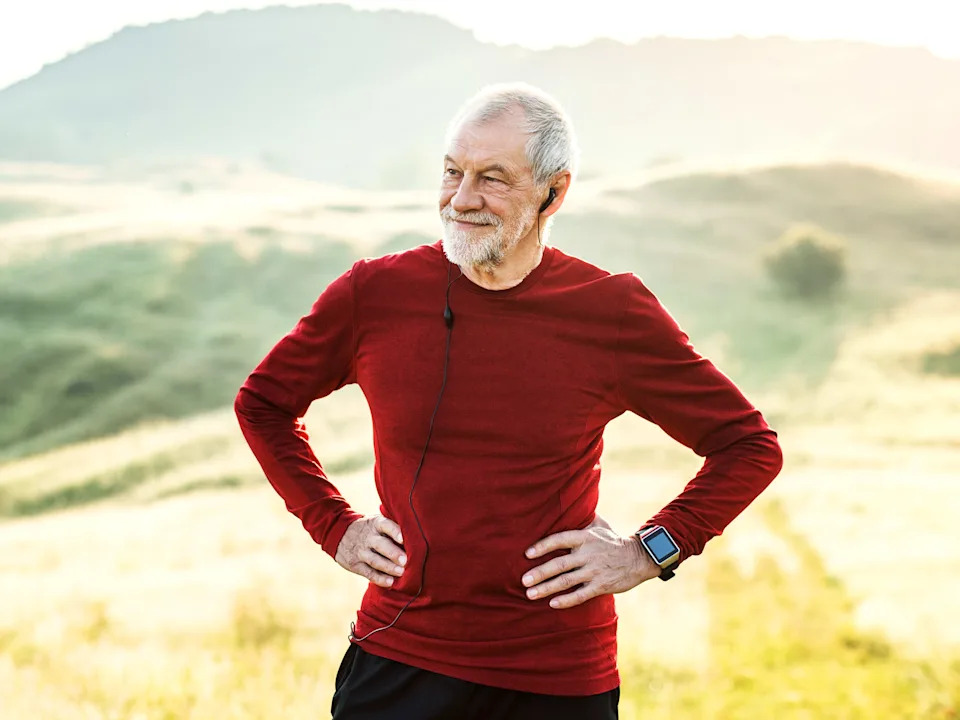 رجل كبير بالخارج يركض ويرتدي قميصًا أحمر ويضع سماعات الرأس بداخله