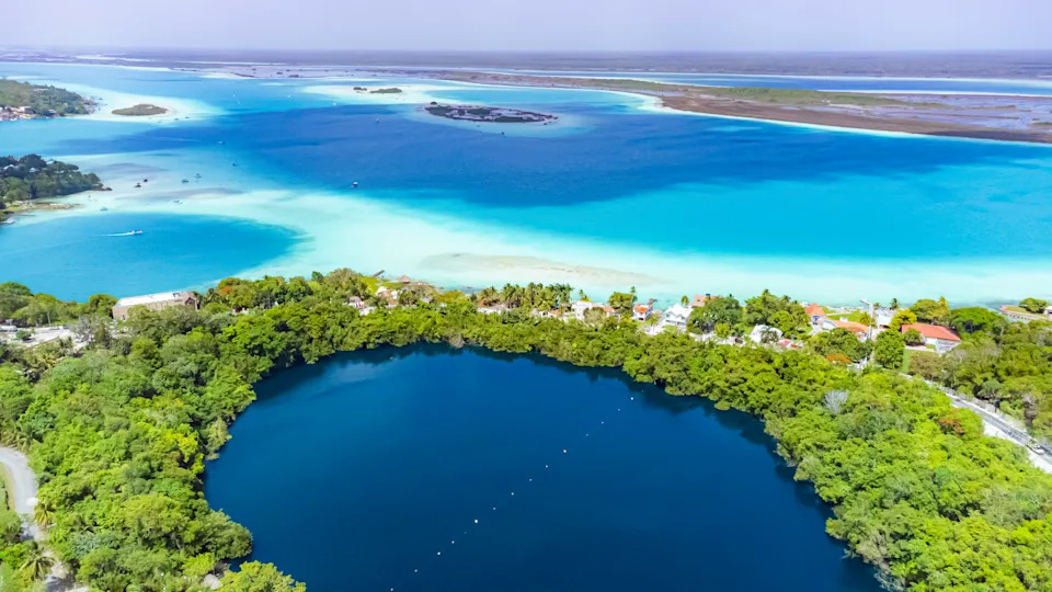 باكالار، المكسيك، كوينتانا رو، البحيرة الزرقاء محاطة بالأشجار والمنازل. البحيرة محاطة بغابة والمنازل على الشاطئ