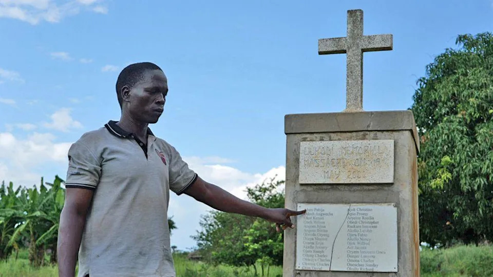 محمد أولانيا يشير إلى نصب تذكاري لمن ماتوا في قرية لوكودي