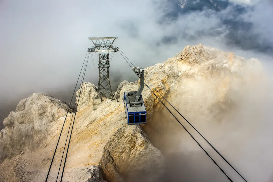 التلفريك معلق فوق أحد جبال الألب. التلفريك ذو لون أزرق ويتحرك نحو أعلى جبل زوجسبيتزي