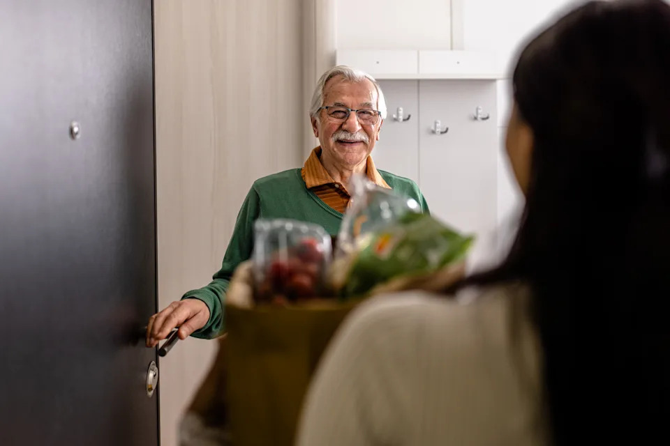 رجل قوقازي سعيد ومبهج يتلقى حقيبة تحتوي على البقالة من متطوع شاب