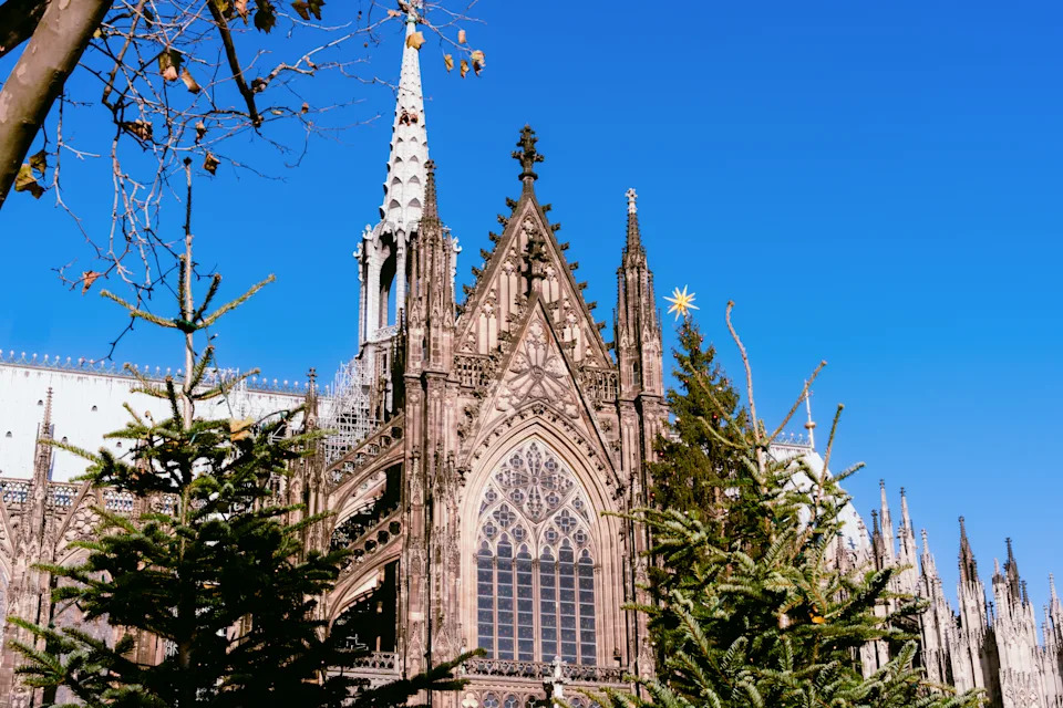 كاتدرائية قوطية بأشجار عيد الميلاد المزخرفة وزخرفة النجوم الاحتفالية تحت سماء الشتاء الزرقاء الصافية وسوق عطلة عيد الميلاد