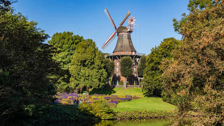 طاحونة خشبية قديمة محاطة بالأشجار والمساحات الخضراء أمام بركة