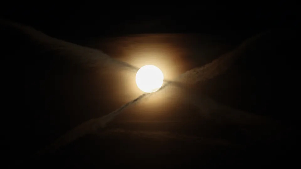 تم تصوير القرص المتوهج للقمر المكتمل وهو يتوهج في سماء الليل السوداء خلف حجاب رقيق من السحابة بينما يشكل مساران للطائرات شكل 