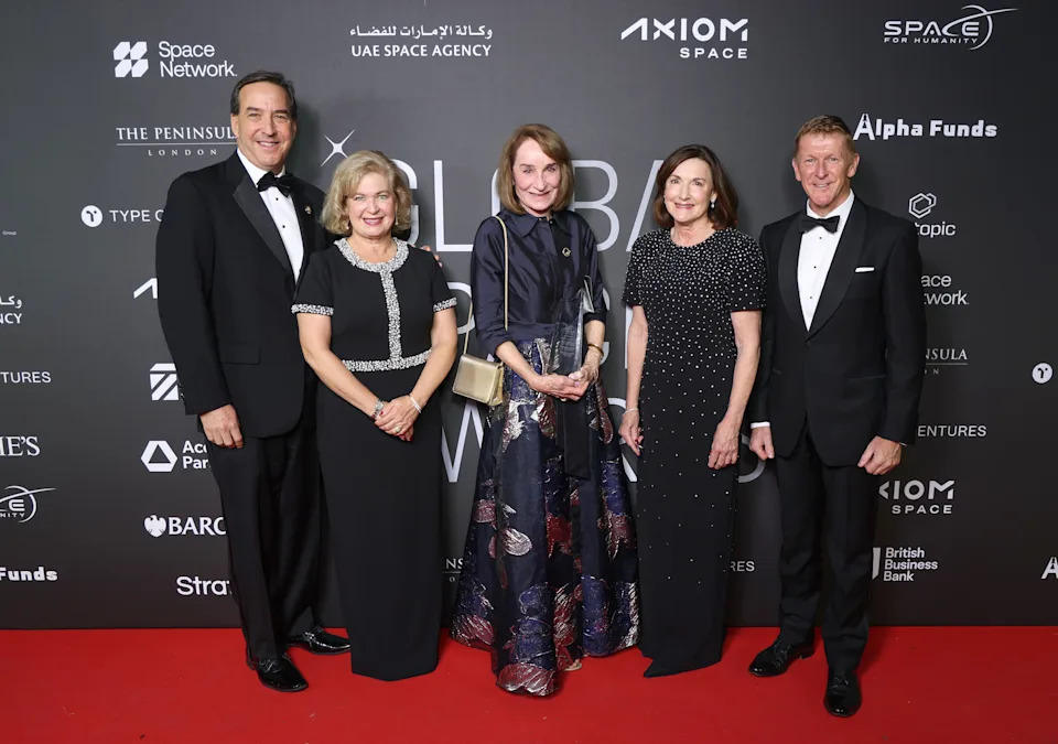 مجموعة من خمسة أشخاص يرتدون البدلات الرسمية والفساتين يقفون على السجادة الحمراء.