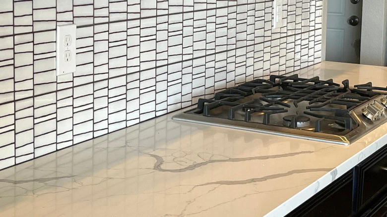 سطح من الرخام مزود بموقد طهي وبلاط باكسبلاش من بلاط الزليج الأبيض.