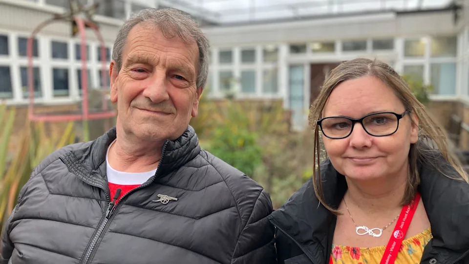 إيان، رجل يرتدي سترة سوداء بسحاب، وسام، امرأة ترتدي قميصًا أصفر ومعطفًا أسود، يبتسمان للكاميرا.