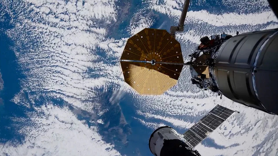 تُرى الأرض وهي تبلغ ذروتها من خلال الغطاء السحابي فوق أرض زرقاء في الغالب بينما تمتد سفينة فضائية راسية إلى الإطار من محطة فضائية