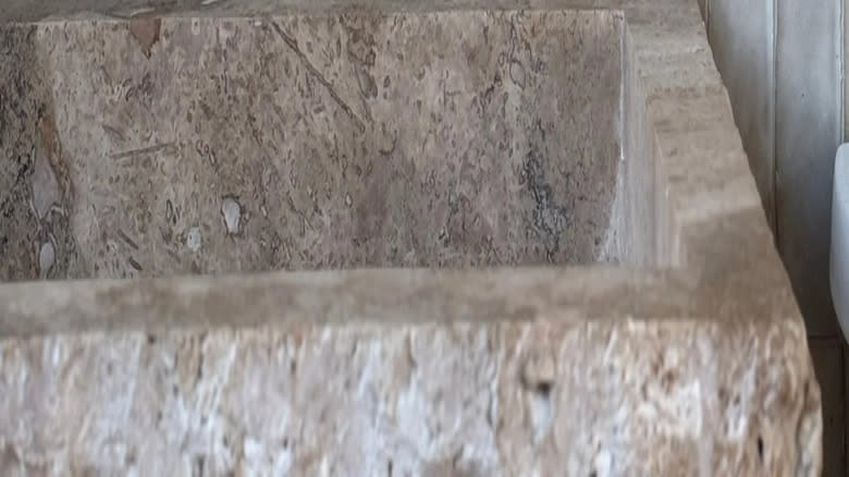 حوض من الحجر الجيري مع بلاط زليج أبيض وصنبور ذهبي ناعم.