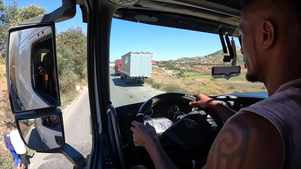 منظر من كابينة شاحنة يظهر طريقًا ضيقًا وبعض المركبات المتوقفة.