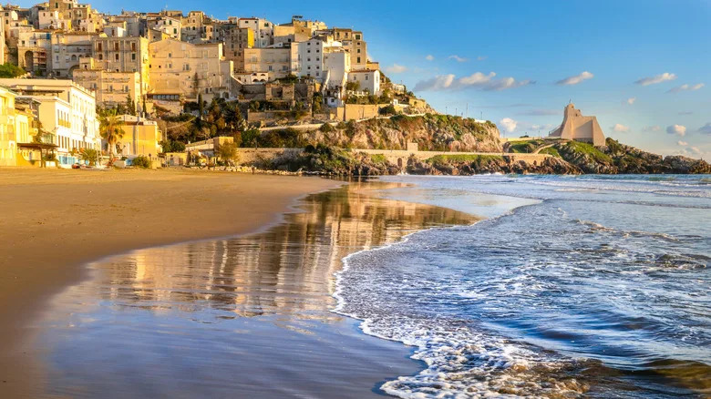 تتلاطم الأمواج على شاطئ رملي مع ظهور مباني سبيرلونجا التاريخية على جانب التل في الخلفية