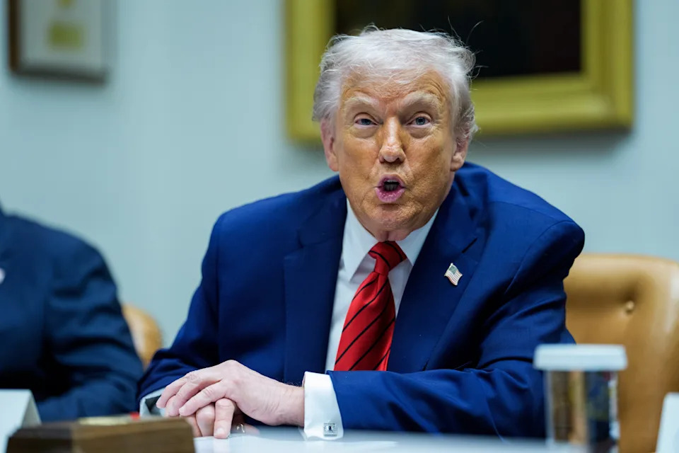 شخص يرتدي بدلة ويتحدث في اجتماع، ويجلس على طاولة. يبدون متحركين ومنخرطين في المناقشة